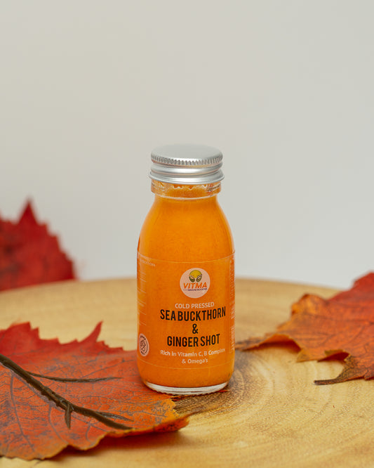 Orange bottle of Seabuckthorn & Ginger Shot on a wooden surface with autumn leaves.
